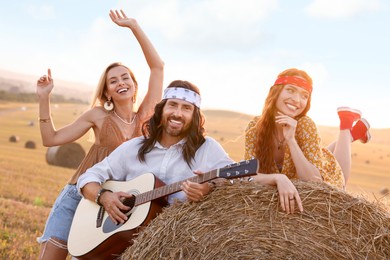 Beautiful hippie women listening to their friend playing guitar in field