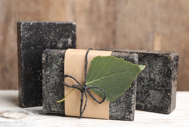 Photo of Natural tar soap on white wooden table, closeup