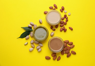 Different types of nut butter and ingredients on yellow background, flat lay