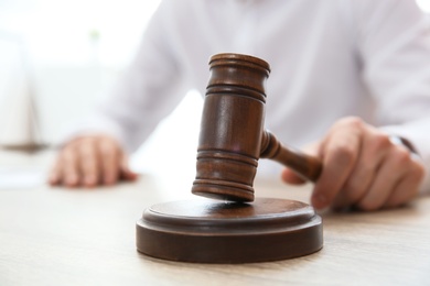 Judge with gavel at table in courtroom, closeup. Law and justice concept