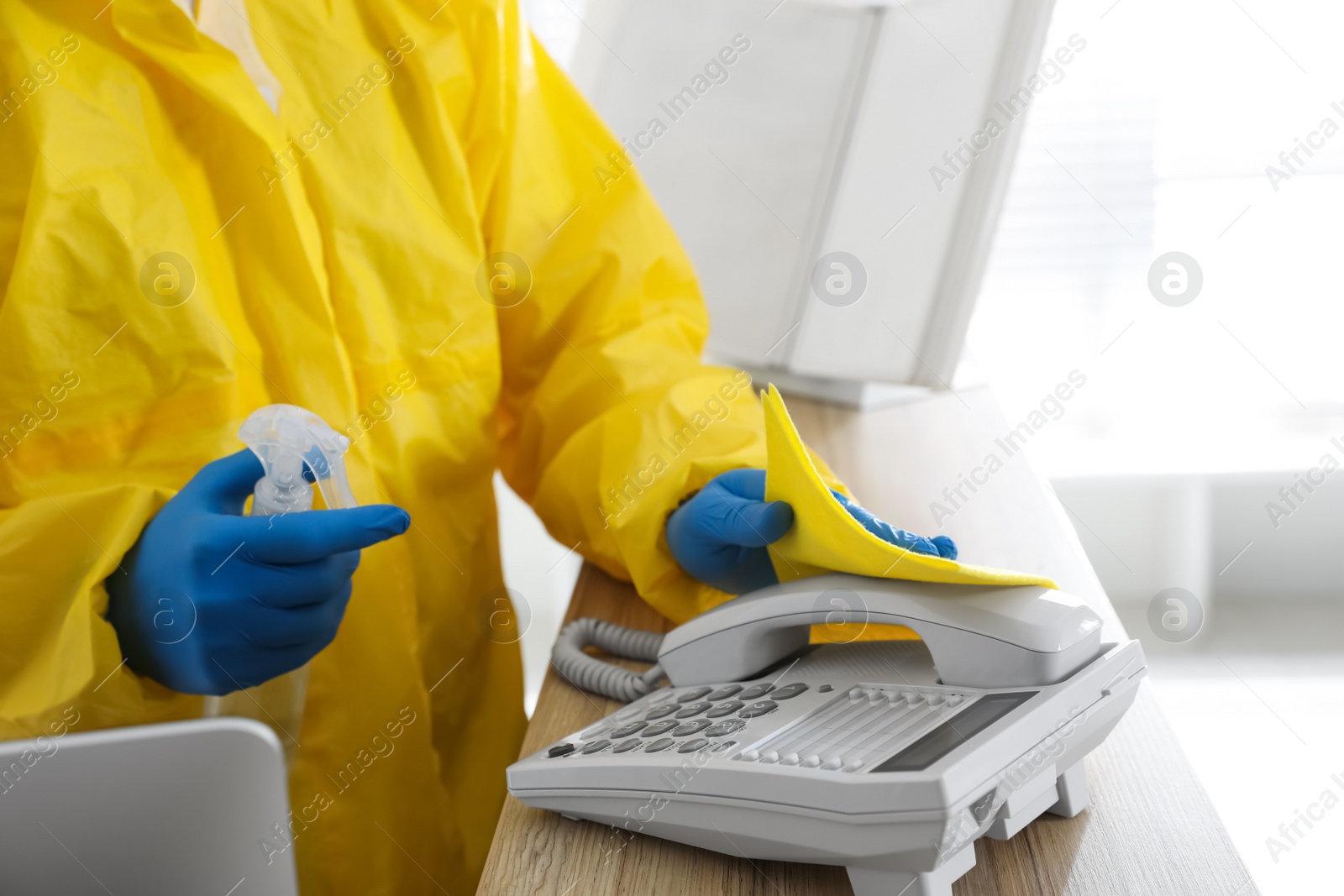 Photo of Employee in protective suit and gloves corded phone indoors, closeup. Medical disinfection