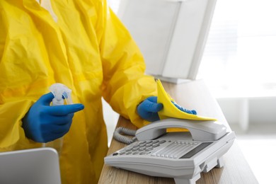 Photo of Employee in protective suit and gloves corded phone indoors, closeup. Medical disinfection