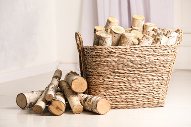Photo of Wicker basket with cut firewood on white floor indoors