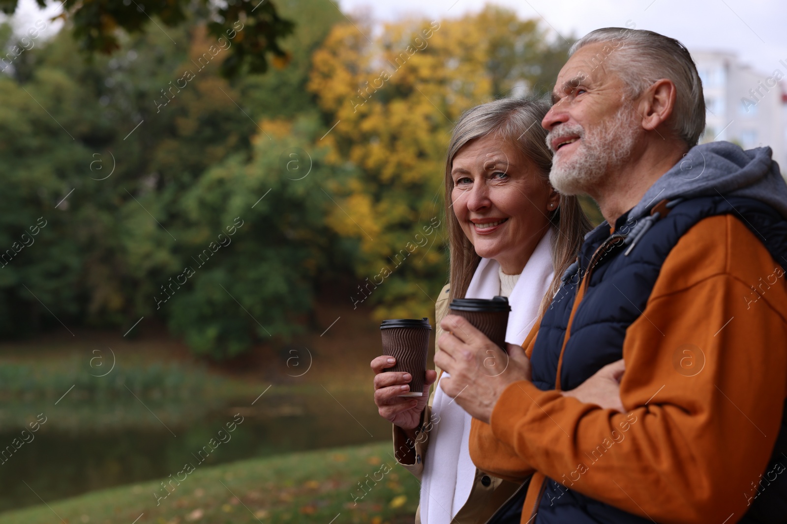 Photo of Affectionate senior couple with cups of coffee in autumn park, space for text