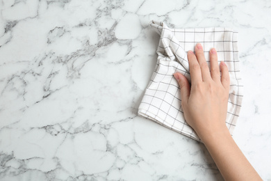 Photo of Woman wiping white marble table with kitchen towel, top view. Space for text