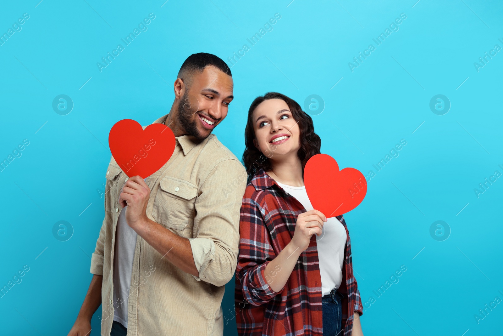 Photo of Lovely couple with red paper hearts on light blue background. Valentine's day celebration