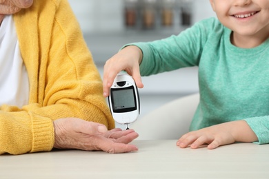 Photo of Senior woman with her grandson using digital glucometer at home, closeup. Diabetes control