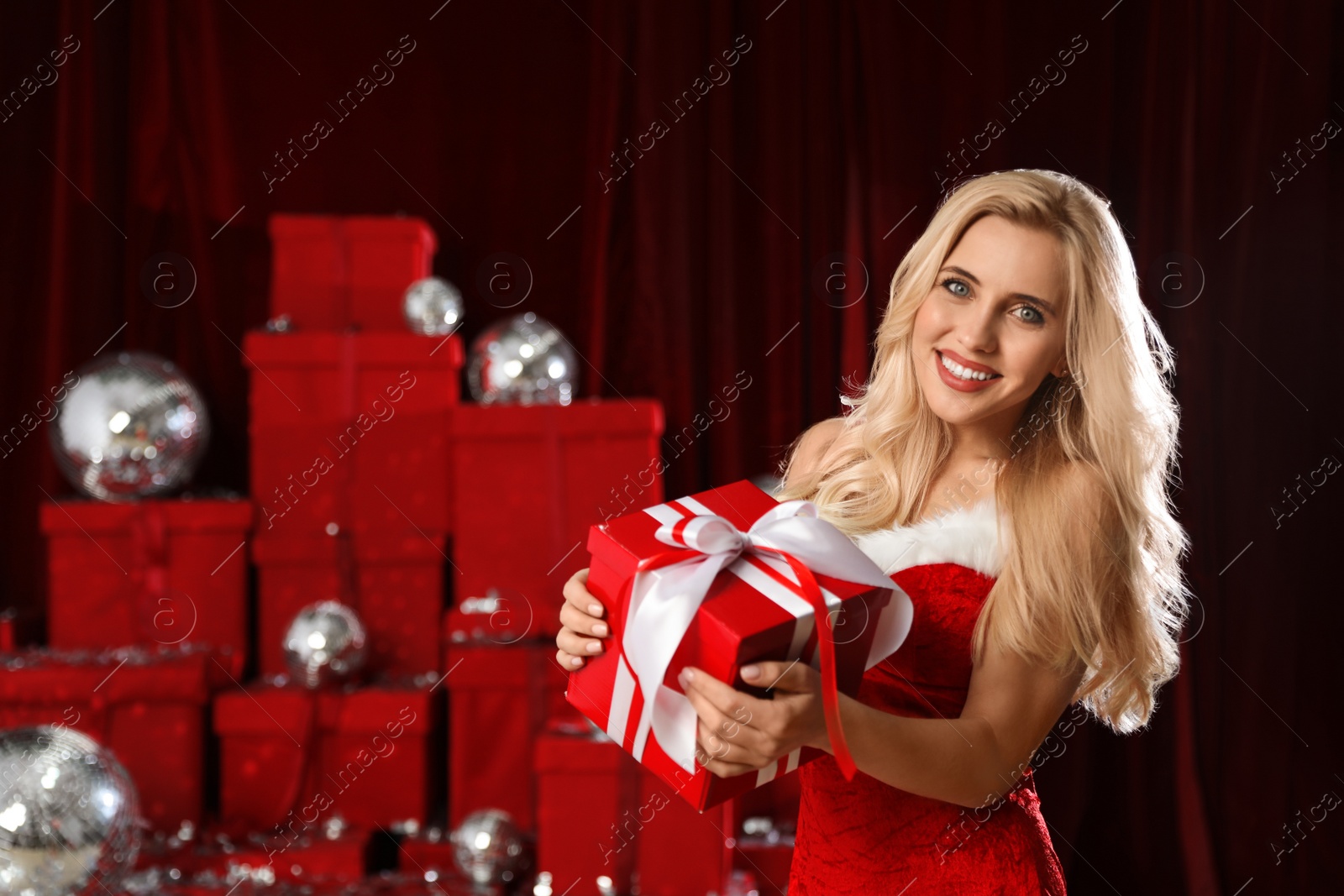 Photo of Beautiful woman with Christmas gift near pile of presents indoors