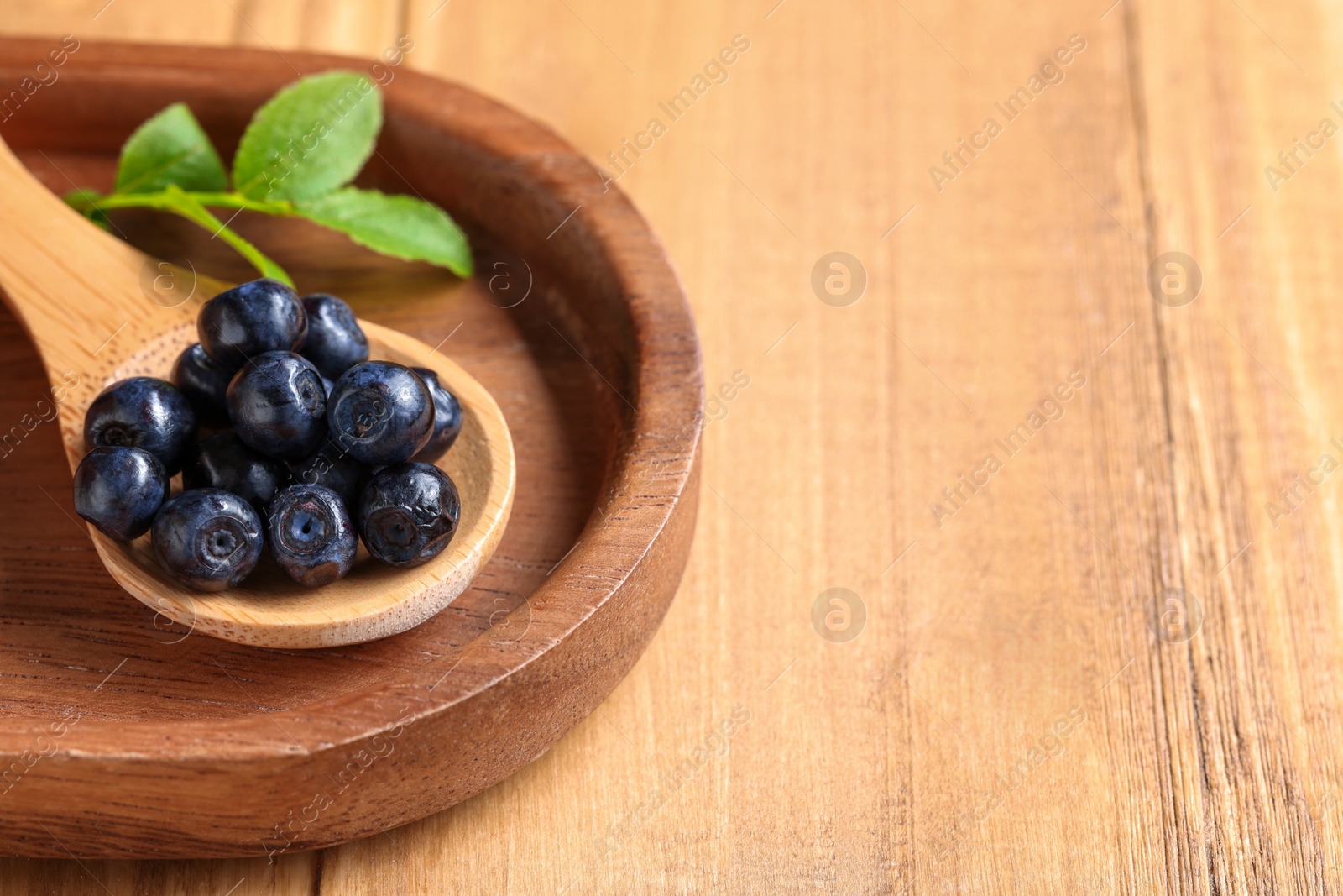 Photo of Spoon with tasty fresh bilberries on wooden table, closeup. Space for text