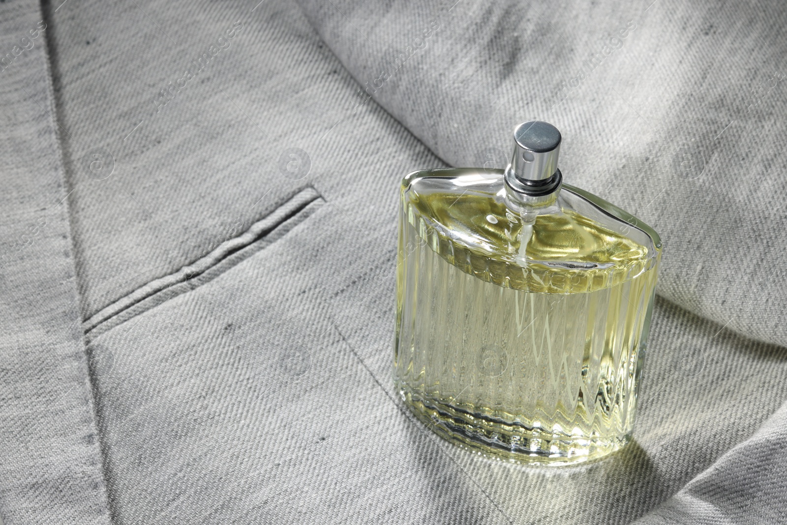 Photo of Luxury men's perfume in bottle on grey jacket, space for text