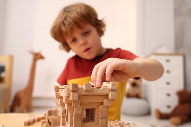 Little boy playing with wooden construction set at table in room, selective focus. Child's toy