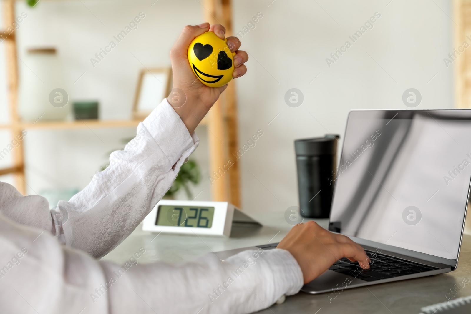 Photo of Woman squeezing antistress ball while working on laptop in office, closeup