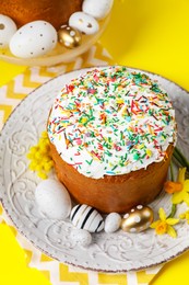 Photo of Traditional Easter cakes with sprinkles, painted eggs and beautiful spring flowers on yellow background