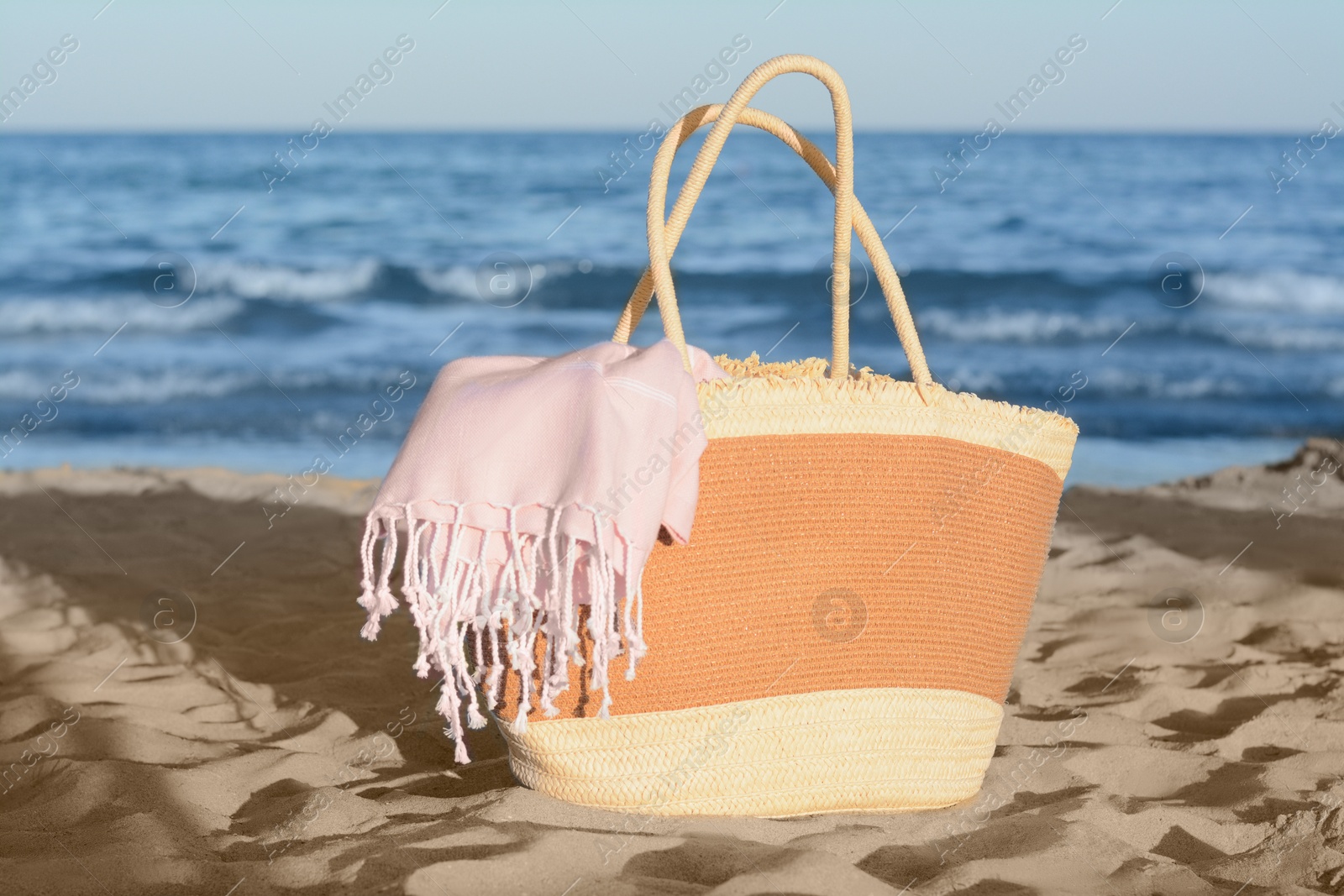 Photo of Stylish wicker bag on sandy beach near sea