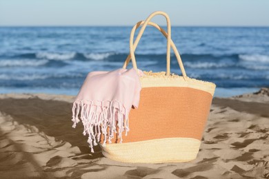 Stylish wicker bag on sandy beach near sea