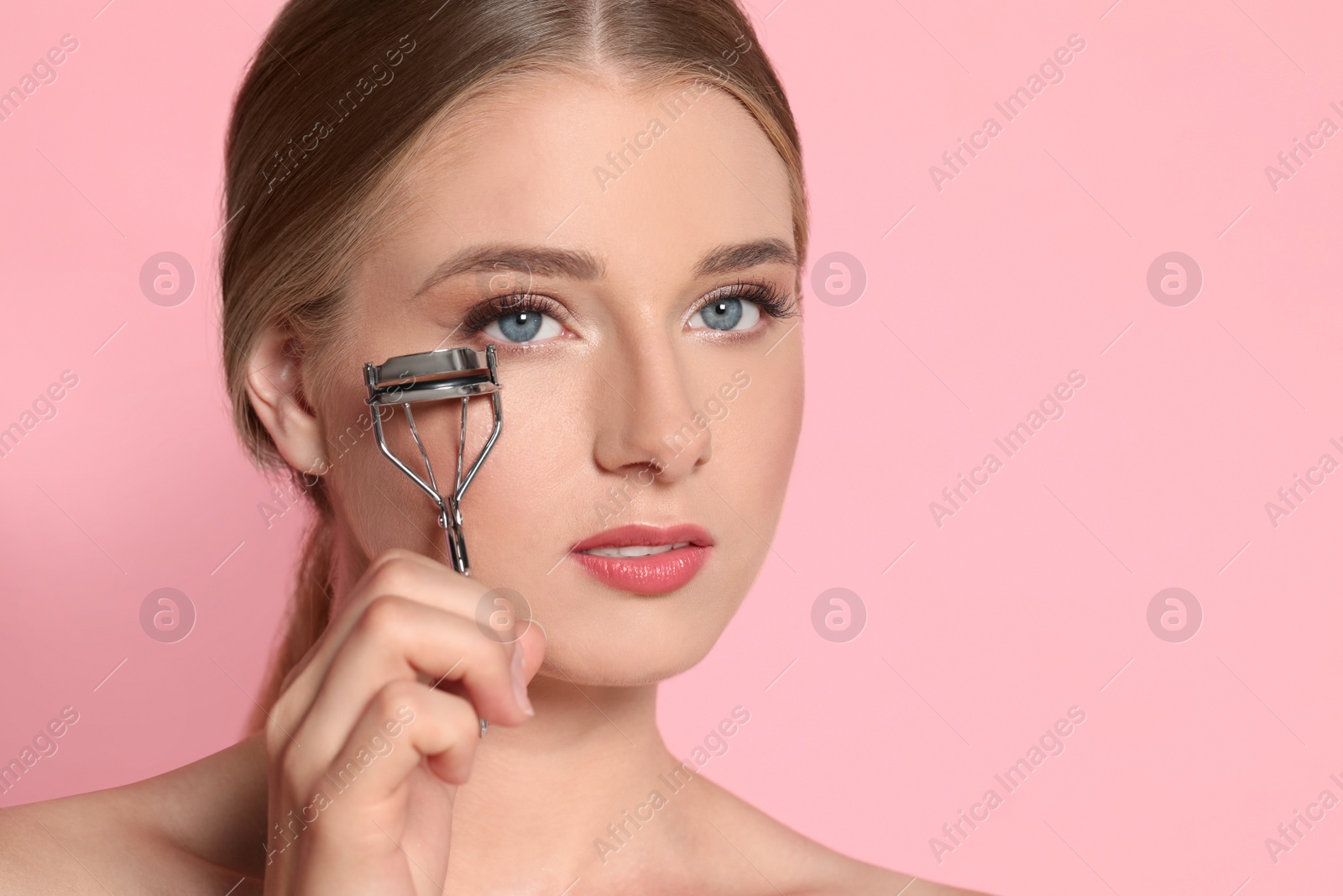 Photo of Young woman with eyelash curler on pink background, space for text