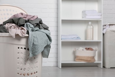 Plastic laundry basket overfilled with clothes indoors. Space for text