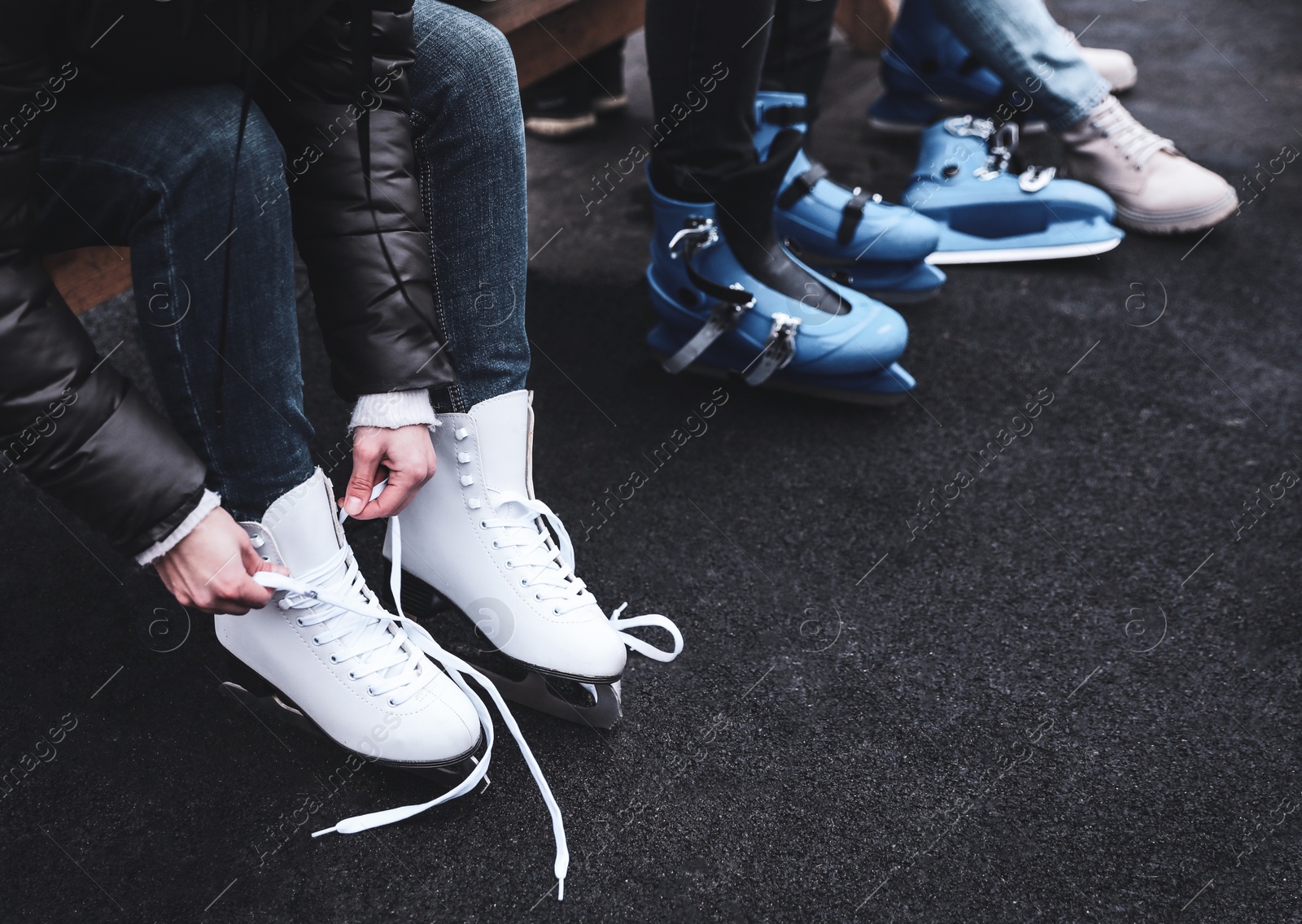 Image of Young woman wearing white ice skates on bench outdoors, closeup