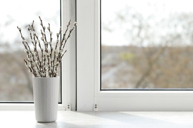 Photo of Beautiful pussy willow branches in vase on window sill indoors, space for text