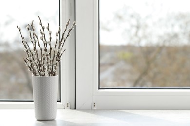 Beautiful pussy willow branches in vase on window sill indoors, space for text