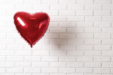 Photo of Red heart shaped balloon near white brick wall, space for text. Valentine's Day celebration