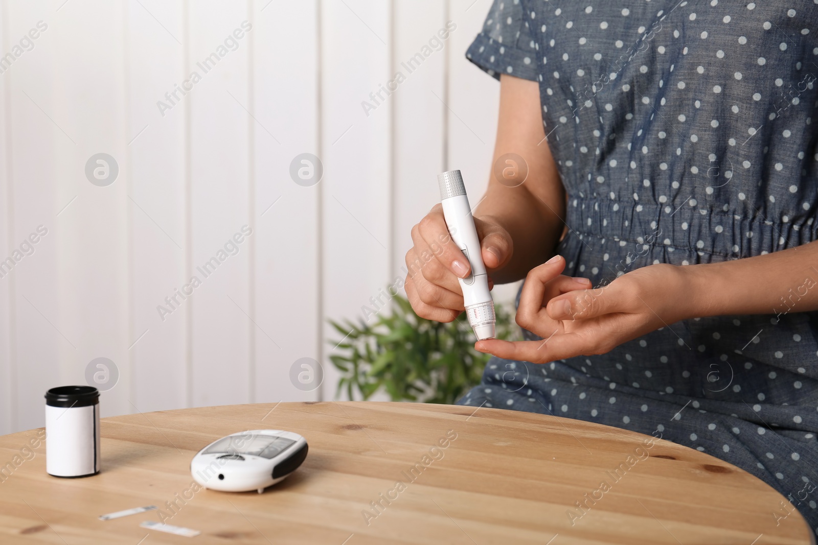 Photo of Woman using lancet pen at table. Diabetes test