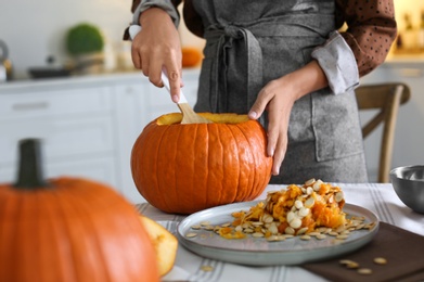 Photo of Woman making pumpkin jack o'lantern at table indoors. Halloween celebration