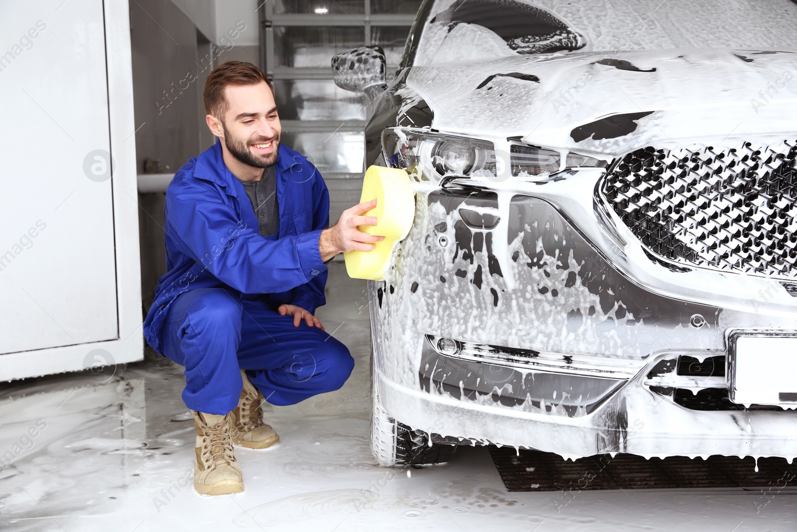 Photo of Worker cleaning automobile with sponge at professional car wash