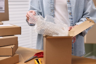 Photo of Post office worker packing parcel at wooden table indoors, closeup