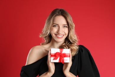 Beautiful young woman with Christmas present on red background