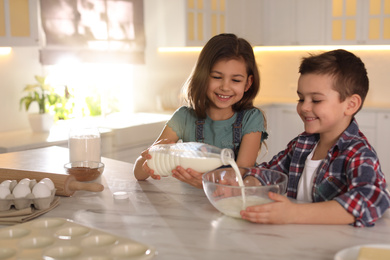 Cute little children cooking dough in kitchen at home