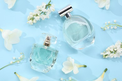 Photo of Luxury perfumes and floral decor on light blue background, flat lay