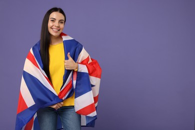 Photo of Happy young woman with flag of United Kingdom showing thumbs up on violet background, space for text