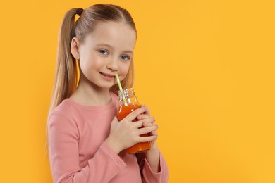 Photo of Cute little girl with glass of fresh juice on orange background, space for text