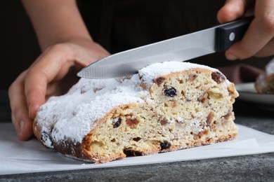 Photo of Woman cutting traditional Christmas Stollen at grey table, closeup
