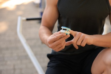 Photo of Man checking pulse with blood pressure monitor on finger after training outdoors, closeup. Space for text
