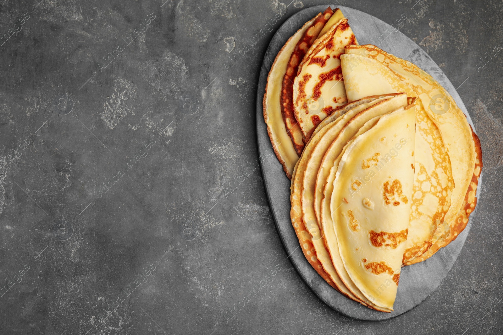 Photo of Fresh thin pancakes on grey table, top view. Space for text