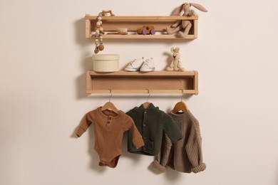 Wooden shelves with baby clothes, toys and accessories on white wall