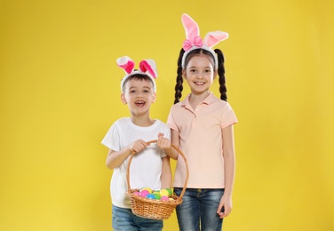 Photo of Cute children in bunny ears headbands holding basket with Easter eggs on color background