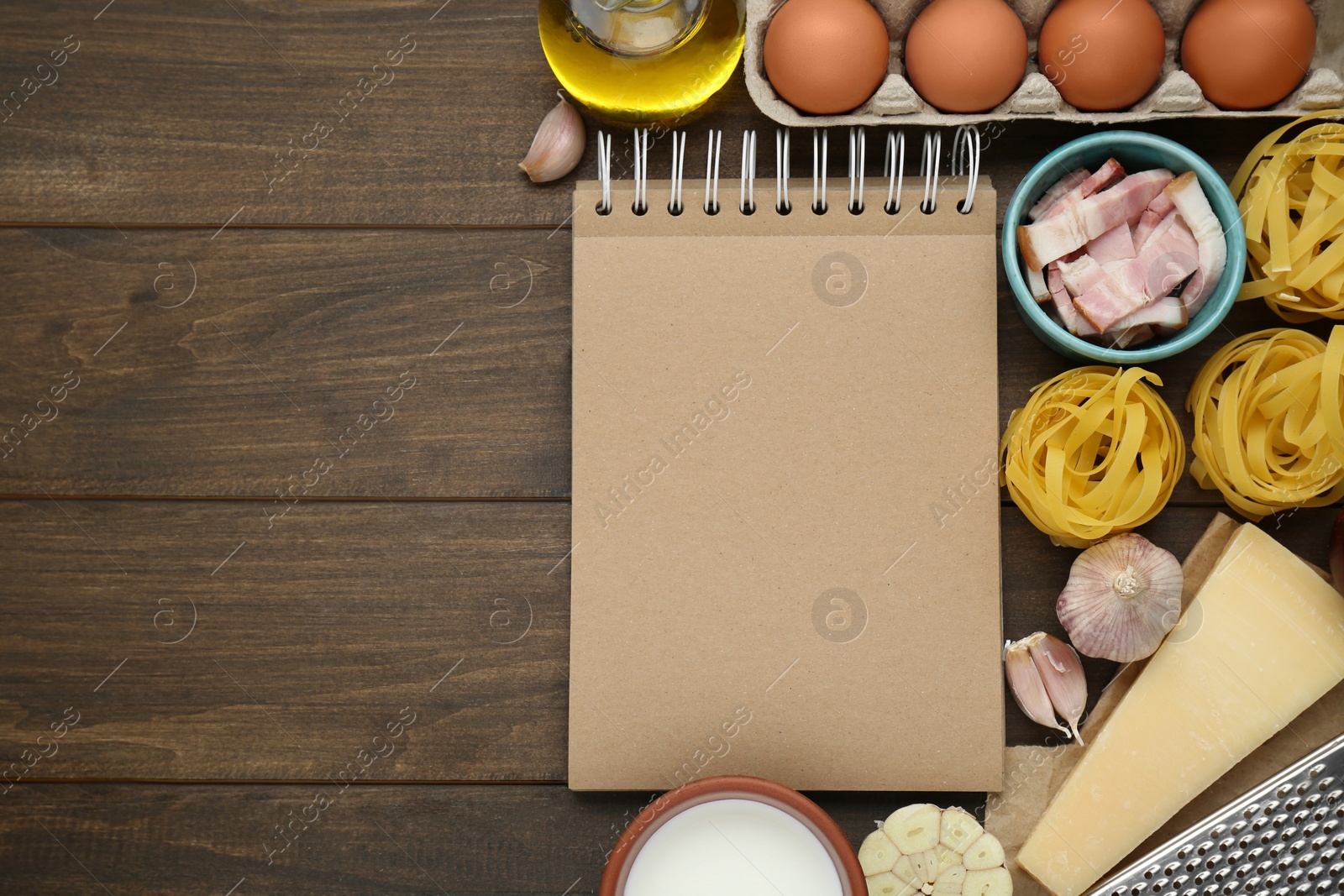 Photo of Blank recipe book and different ingredients on wooden table, flat lay. Space for text