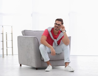 Handsome young man sitting in armchair indoors. Space for text