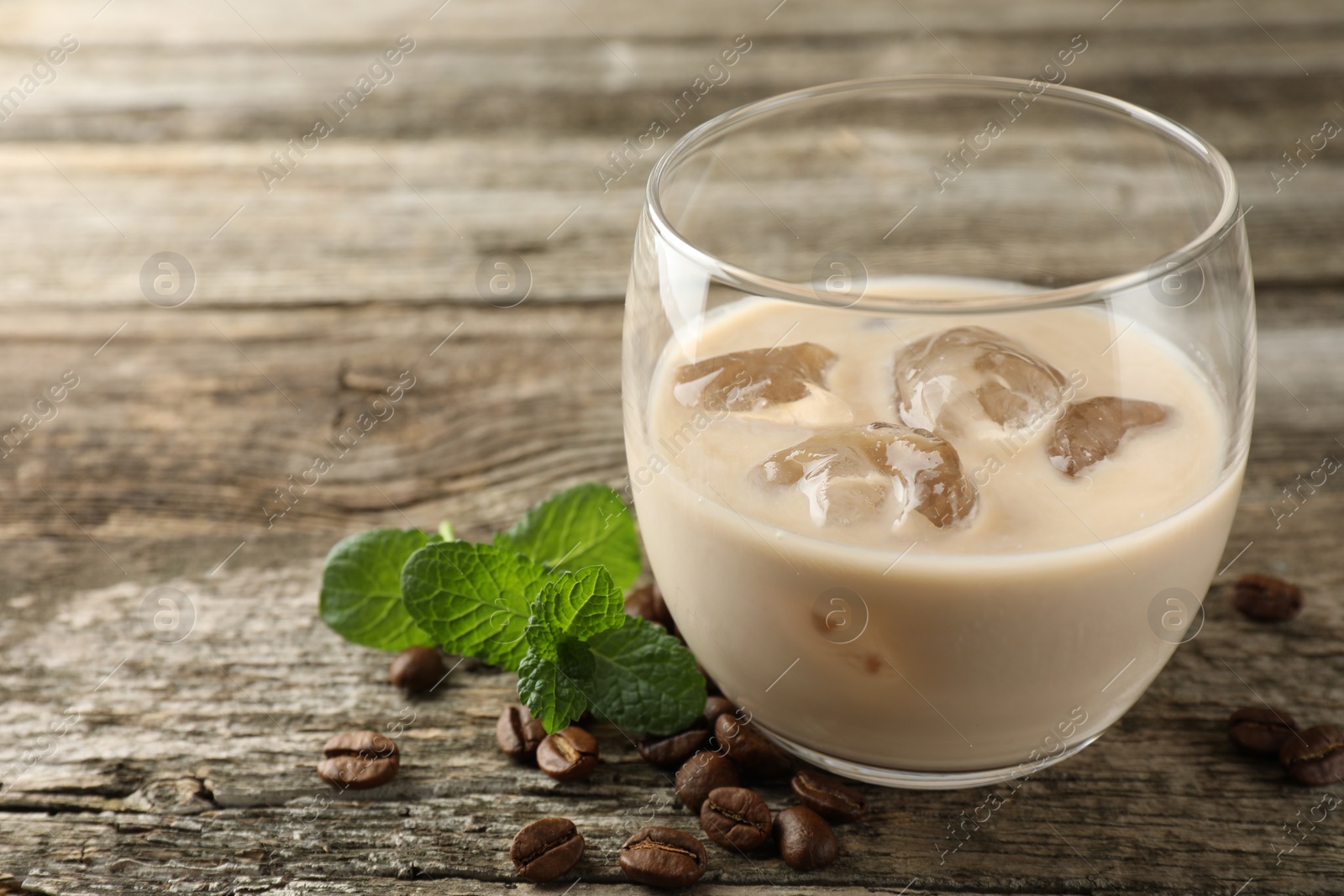 Photo of Coffee cream liqueur in glass, mint and beans on wooden table, closeup