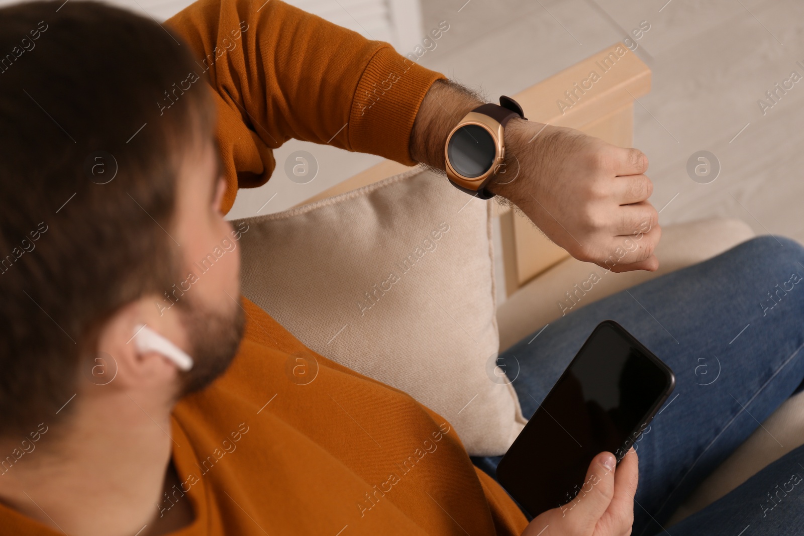 Photo of Young man with smart watch, phone and earphones at home, above view