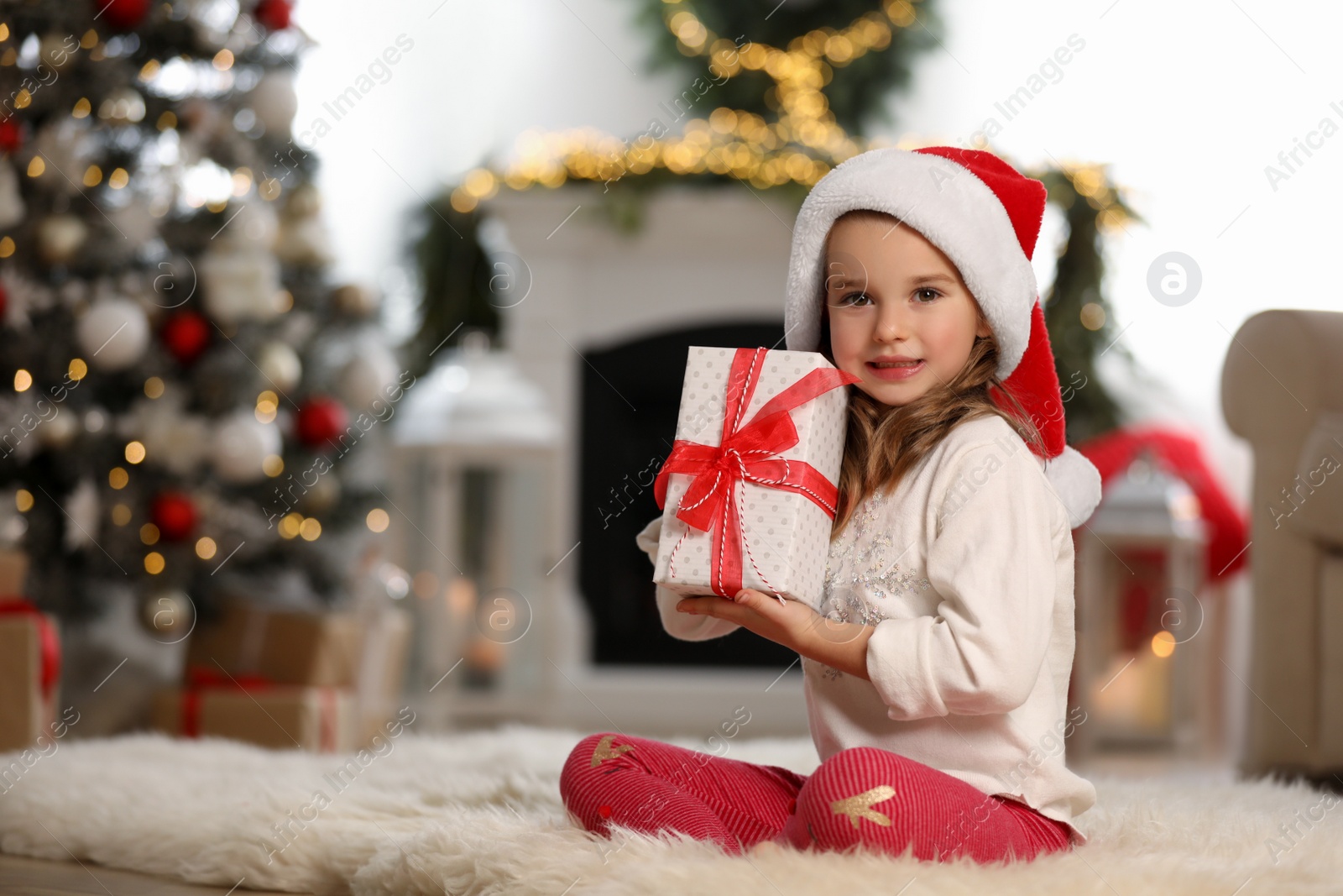 Photo of Cute little girl holding gift box in room decorated for Christmas