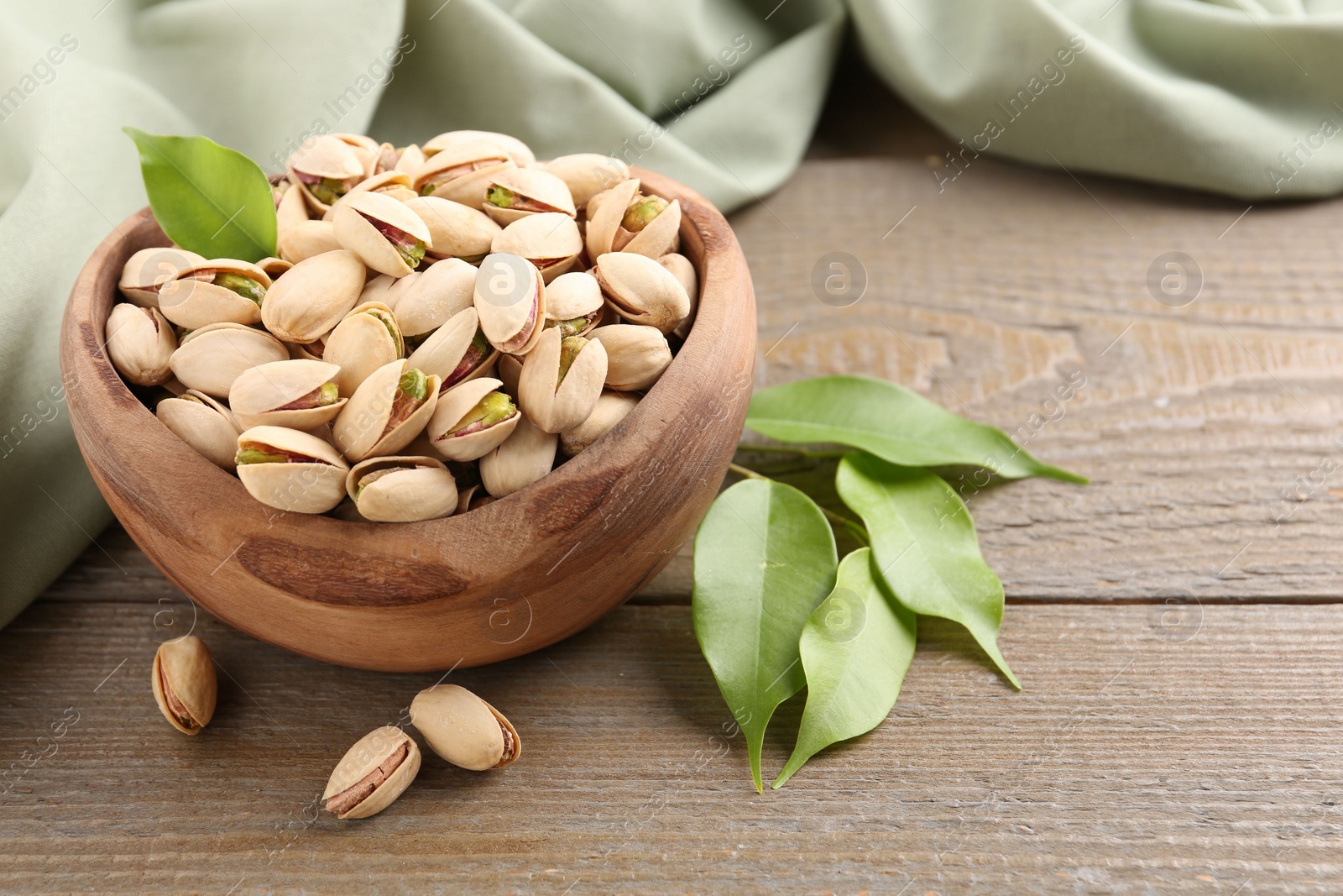 Photo of Delicious pistachios in bowl on wooden table, closeup