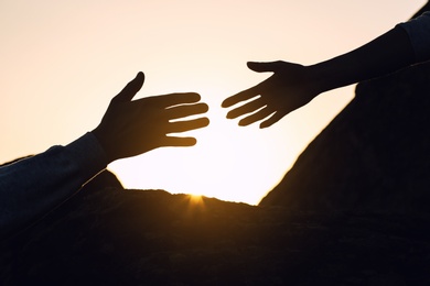 Photo of Silhouettes of man and woman helping each other to climb on hill against sunset, closeup