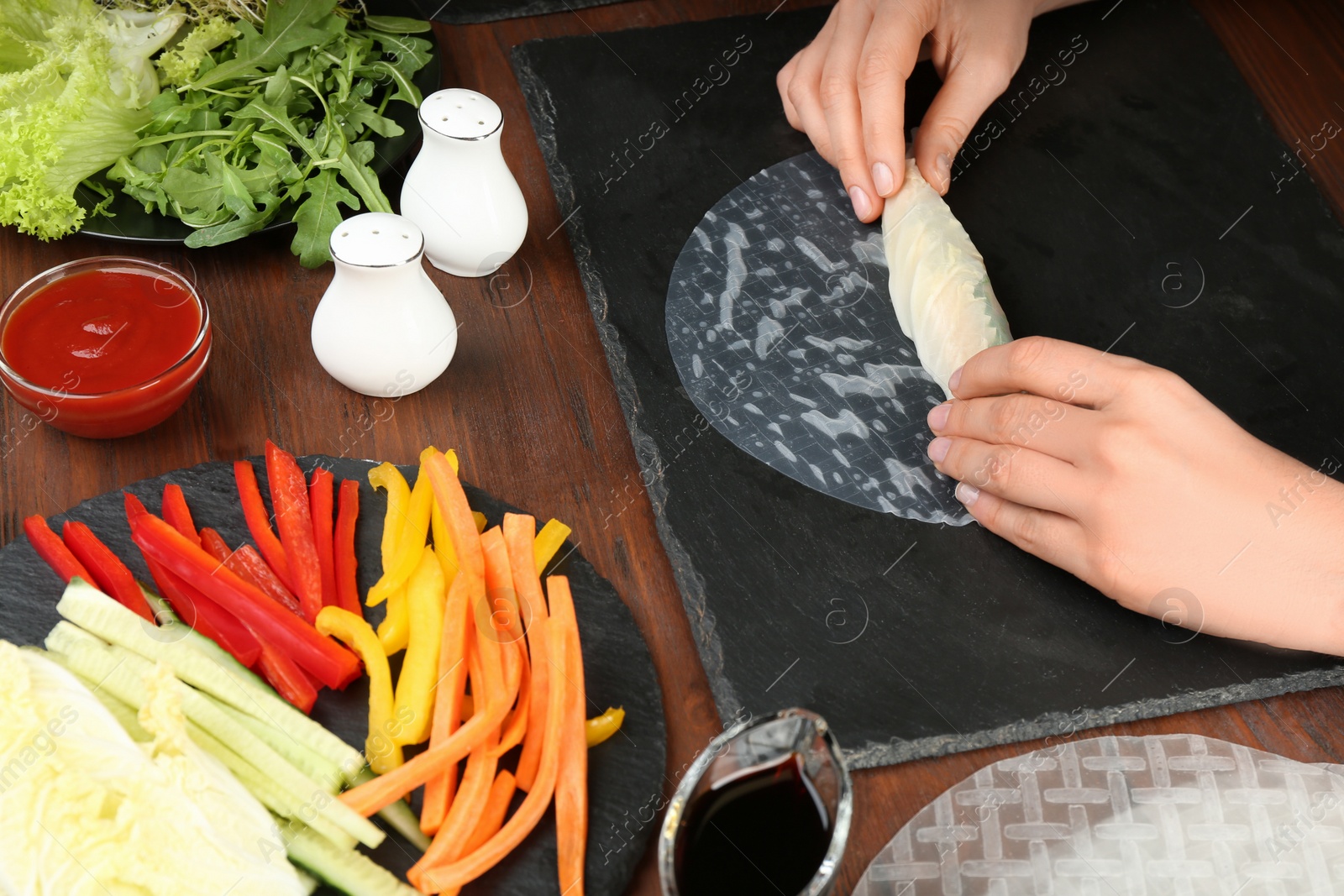 Photo of Woman making rice paper roll at wooden table, closeup