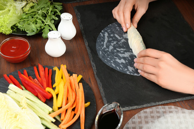 Woman making rice paper roll at wooden table, closeup