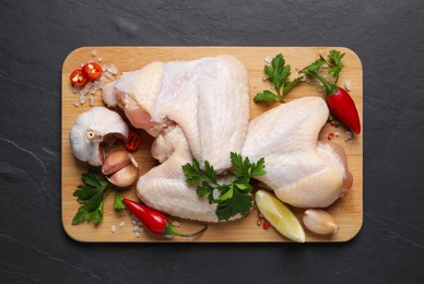 Photo of Wooden board with fresh raw chicken wings and other products on black table, top view