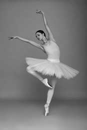 Image of Young ballerina practicing dance moves on light grey background. Black and white effect